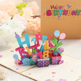 Colorful 'Happy Birthday' pop-up card with balloons and presents on a white surface.