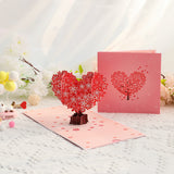 Pop-up card with heart-shaped tree design on a white surface with flowers in the background