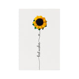 Three handmade greeting cards with preserved flower arrangements, each in different colors, attached to the cards with a pin, displayed on a wooden surface with plants in the background.
