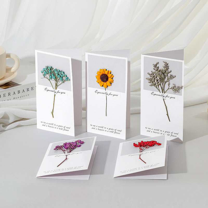 A selection of handmade preserved flower cards displayed on a neutral background, each featuring a different arrangement of preserved flowers.