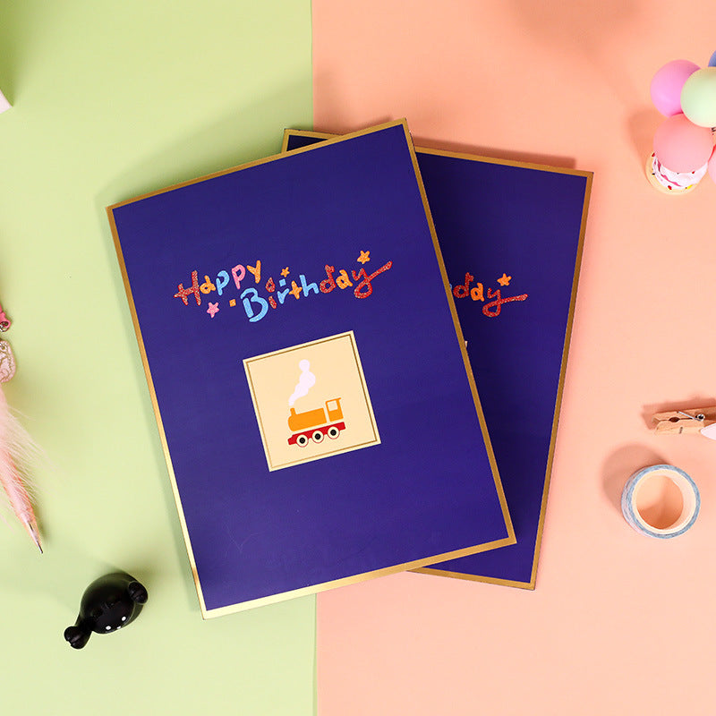 Two blue birthday cards with colorful text and a small illustration on a pink and green background.