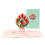 A 3D pop-up greeting card with a miniature bouquet of lilies in a red and white striped pot, displayed next to a matching envelope with a floral design.