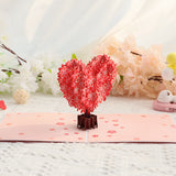 3D heart-shaped floral pop-up card on a white surface with flowers in the background