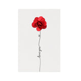 Three handmade greeting cards with preserved flower arrangements, each in different colors, attached to the cards with a pin, displayed on a wooden surface with plants in the background.