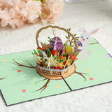Easter-themed pop-up card with a basket of eggs and flowers on a light green background.