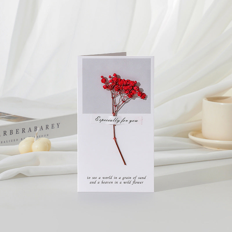 Greeting card with red flowers and text on a white surface with books and candles.