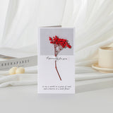Greeting card with red flowers and text on a white surface with books and candles.